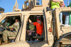 Two people in military uniforms in a humvee during a parade.