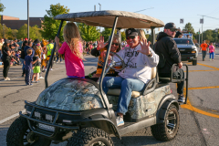 Woman sitting in golf cart waving to crowd at parade.