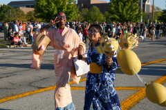 Two people standing on a street holding balloons during a parade.
