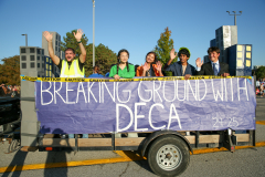 People holding sign that says "breaking ground with deka" at a parade.