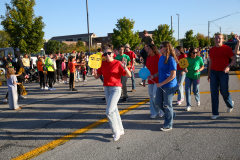People in red shirts walking across a road at a parade.