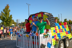 People celebrating at a parade, riding in a colorful truck decorated to look like a Lego car.
