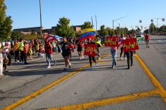 People in a parade holding signs and flags, walking down a street.