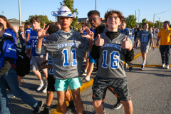 Two young men in football uniforms giving thumbs up, standing on a street during a parade.