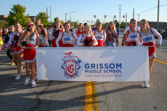 Group of cheerleaders posing for a photo at the end of a parade, holding a banner that reads 'Grisom High School'.