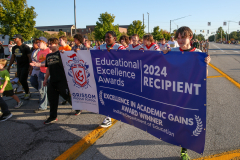 People marching in a parade holding a banner that reads "2040 EXCELLENCE AWARDS RECIPIENT" and "Education