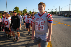 Young boy in football uniform standing amidst a group of people.