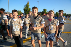 Three young boys wearing football jerseys standing together in front of a crowd.