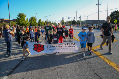 People walking down street holding banner that reads "241004 HOCO Parade Floats".