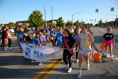 Children in school uniforms marching down street in parade.