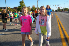 Two young girls walking down a street during a parade, smiling and enjoying themselves.