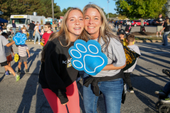 Two women posing for a picture at a parade, one holding a paw print sign.