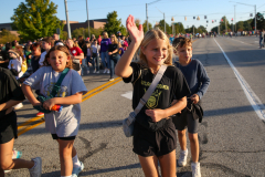 Girl in black shirt waving at camera during parade.
