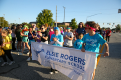 People participating in a parade, holding signs and banners, including one for "Else Rogers Elementary School".