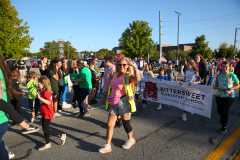 People walking in a parade, some carrying signs and backpacks, others wearing colorful clothing, all smiling and enjoying