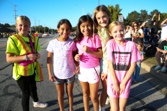 Five young girls in pink shirts posing for a picture at a parade.
