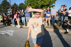 Girl in a tan shirt standing on sidewalk at parade.