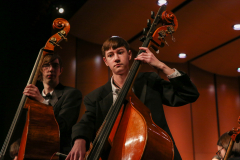 Two men playing cellos on stage in a concert hall.