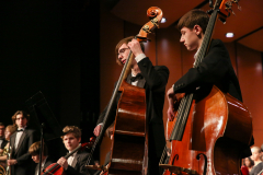 Two musicians playing cellos on stage in front of an audience.