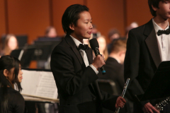 Man in a tuxedo on stage holding a microphone.