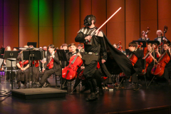 A person dressed as Darth Vader on stage with an orchestra.