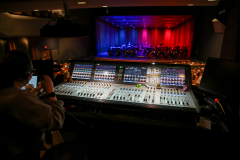 Person operating a large audio mixing console in a theater during a performance.
