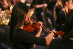 Woman playing violin on stage in front of audience.