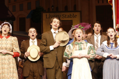 Theatrical cast of a musical production, performing on stage, dressed in period costumes, posing for a group photo.