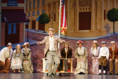 Theatrical performance of a musical production featuring actors in period costumes on stage.