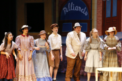 Theatrical cast of "Music Man" on stage in costumes, performing a musical number.