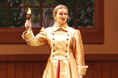 Woman in a gold dress holding a torch on stage.