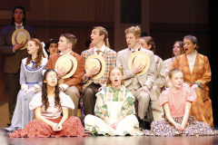 A group of people on stage dressed in costumes, posing for a picture, likely actors performing in a musical production.