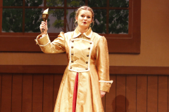 Woman in gold dress on stage holding microphone.
