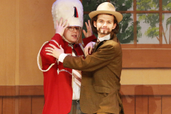 Two men on stage, one in a red jacket and hat, the other in a brown suit and top hat, performing together.