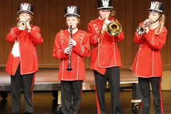 Five musicians in red uniforms playing instruments on stage.