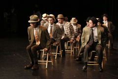 Group of people dressed in vintage clothing on stage, performing as a band.