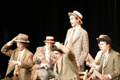 Theatrical performance of a group of actors dressed in vintage costumes, posing for a picture on stage.