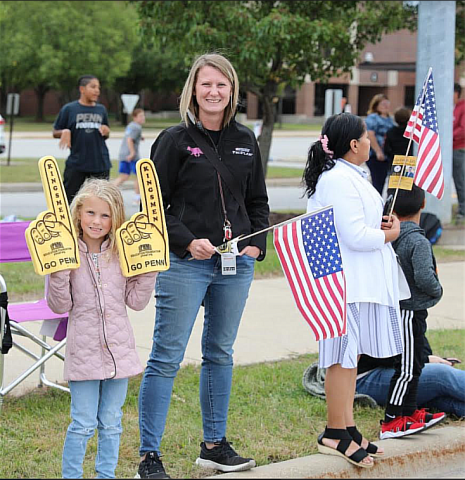 Woman in a white shirt holding two foam fingers, one with a flag design, standing next to a girl holding a similar foam