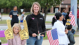 Woman in a white shirt holding two foam fingers, one with a flag design, standing next to a girl holding a similar foam