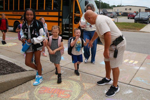 students getting off school bus fist bumping school custodian