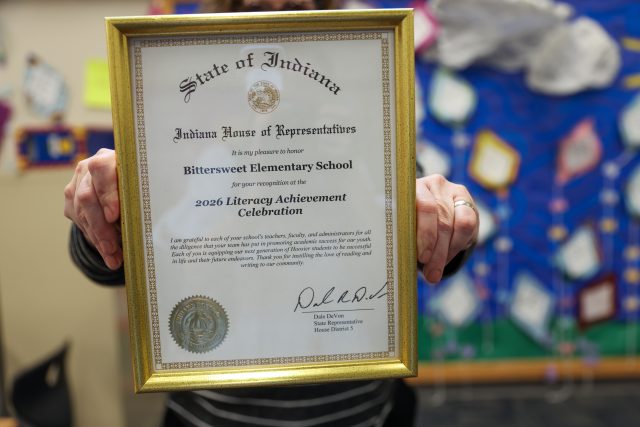 Person holding a framed award in front of a colorful wall.