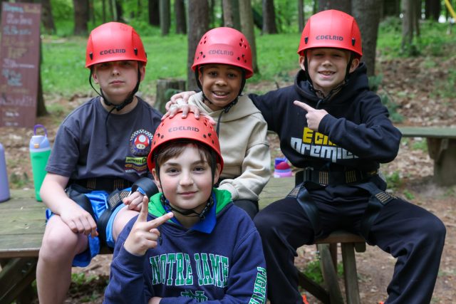 Four children in helmets posing for a picture at an outdoor activity center.