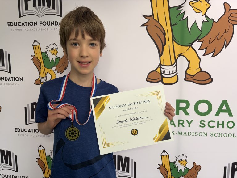Young boy holding a medal in front of a sign for a school. The sign says "national mathematics".