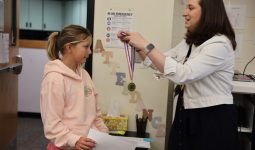 Woman in a white shirt pinning medal on girl's shirt.