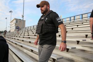 Man in black vest standing on bleachers, looking to his right.