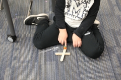 A young child sitting on the floor, holding a small orange pumpkin in their hands, working on a homemade catapult.