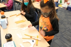 Young girl in a classroom setting working on pumpkin catapults, likely for Halloween.