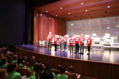 Team of six students participating in a spelling bee competition on stage.