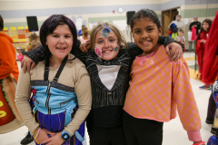 Three children posing together in a school setting, dressed in costumes that resemble anime characters, smiling and looking
