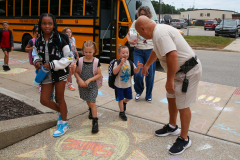 School bus driver greeting children at a crosswalk.